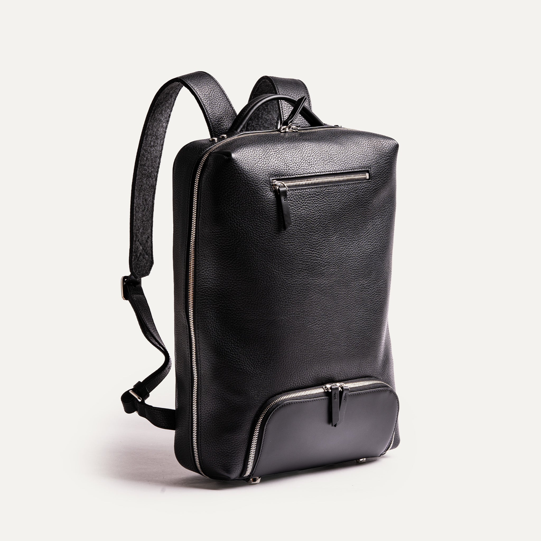 sac à dos en cuir noir avec une texture de grainée, offrant un compartiment principal et une poche frontale plus petite, tous deux avec des fermetures éclair.