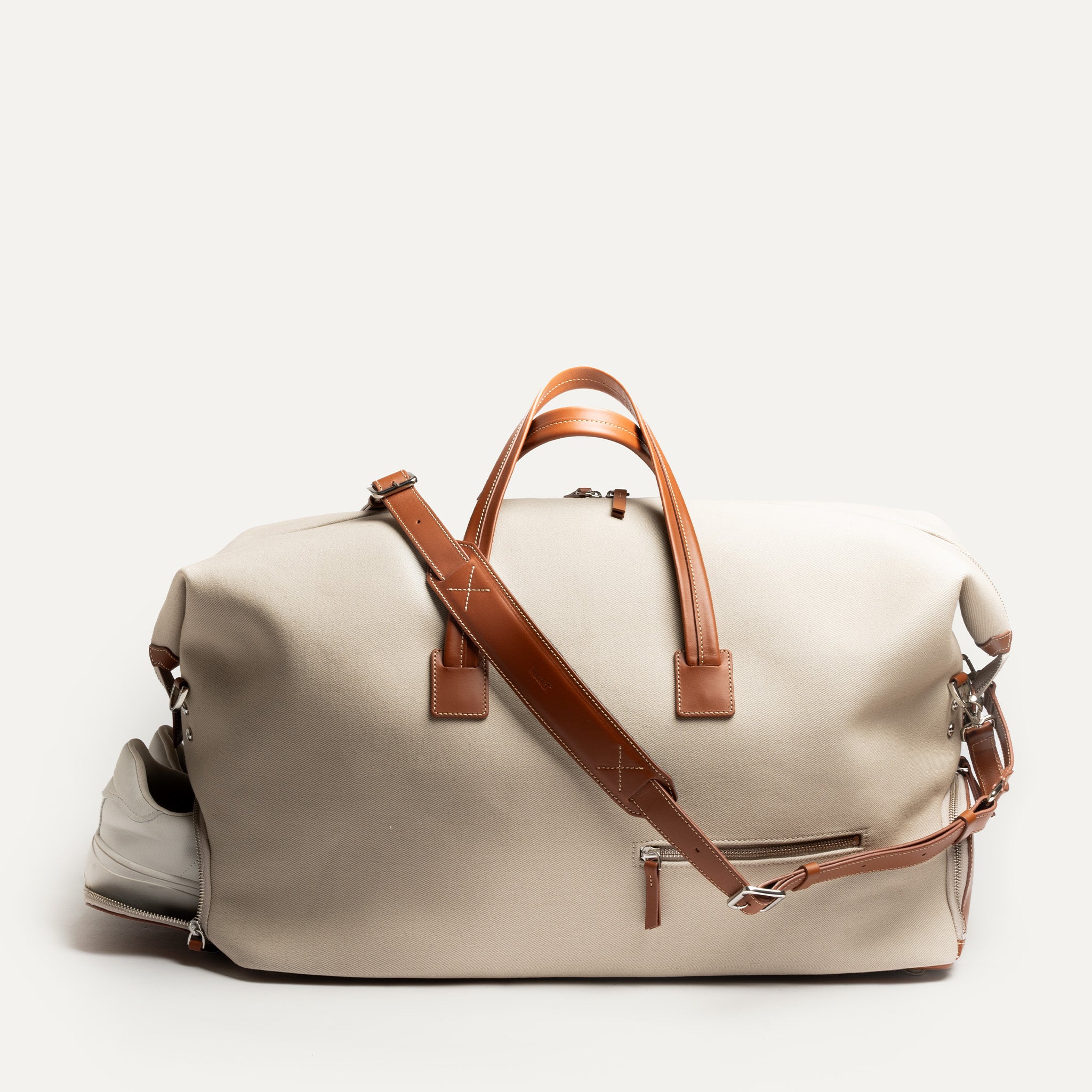 Ce sac de voyage en toile sable et cuir camel est parfait pour vos escapades. Il comprend une poche pour chaussures et une bandoulière réglable pour un confort optimal. Les poignées en cuir ajoutent une touche de sophistication et de confort pour la prise en main. 