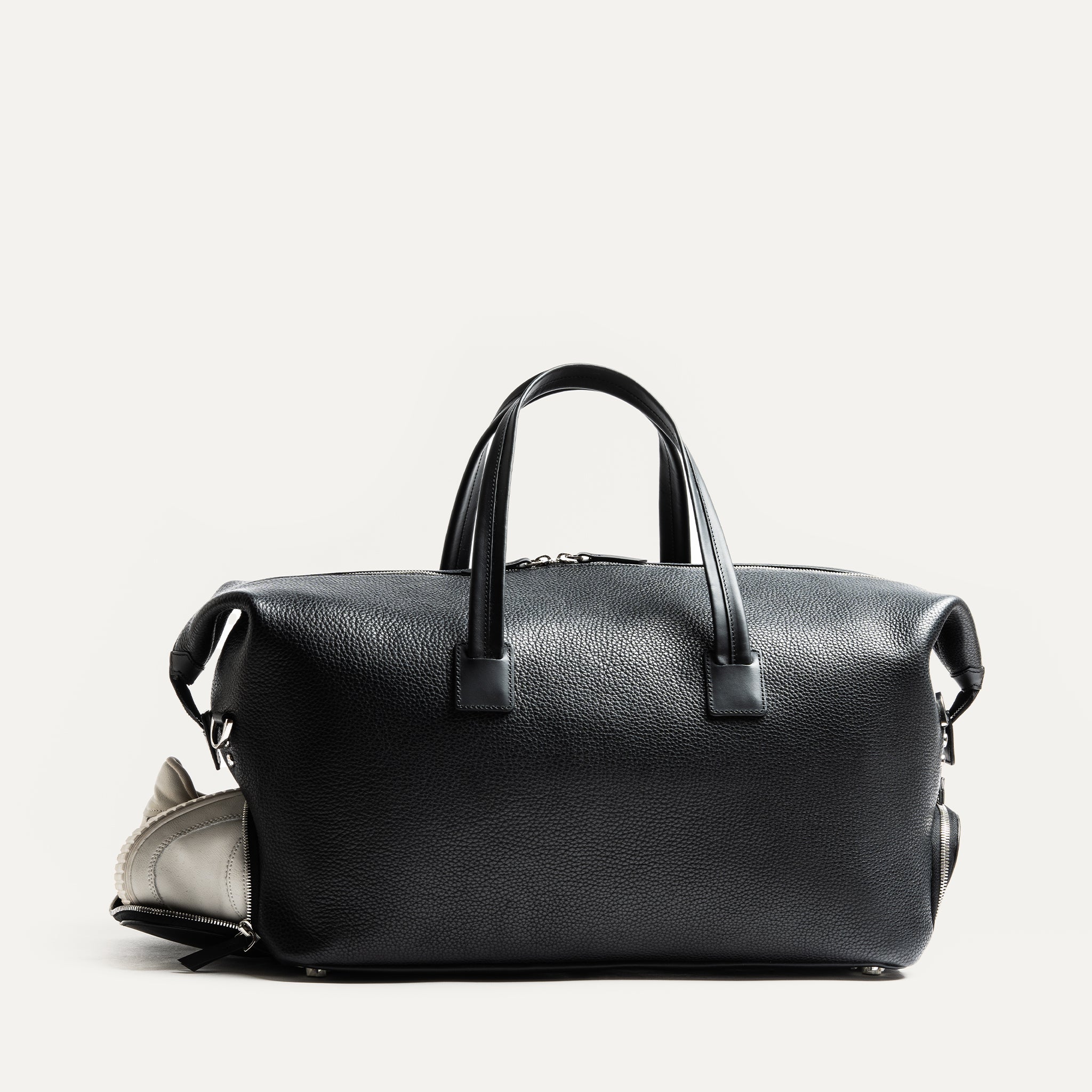 Ce sac de voyage en cuir noir est idéal pour les voyages courts. Il offre un espace de rangement pour vêtements et une poche pour ordinateur portable. Les poches extérieures permettent de ranger facilement chaussures et trousse de toilette. Un sac élégant et pratique pour toutes les occasions.