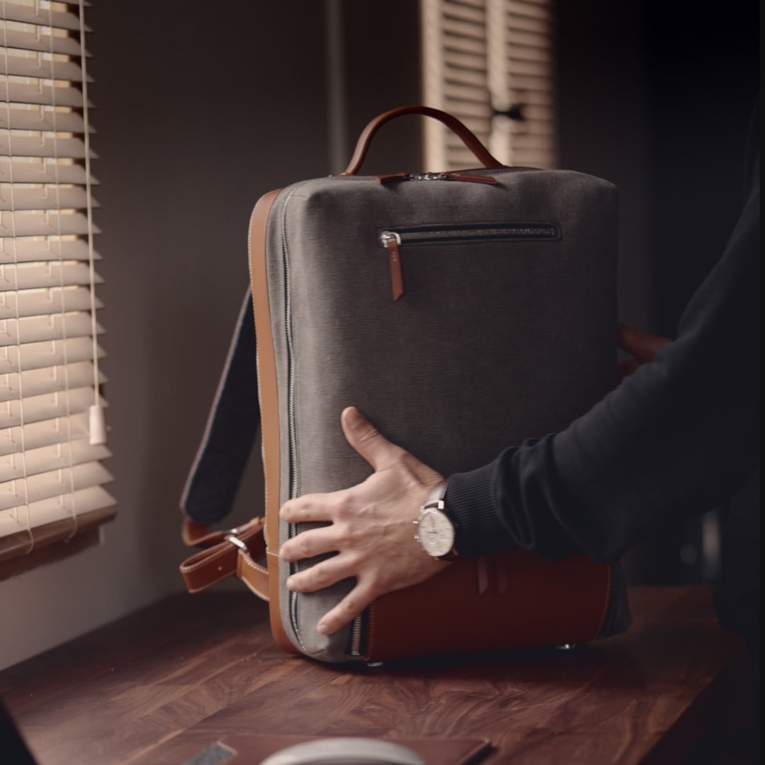 ce sac à dos pour homme est en cuir marron et toile grise. Il est élégant, fonctionnel et idéal pour les déplacements professionnels de courte durée. Les anses ajustables en cuir et la feutrine recyclée à l’intérieur offrent un confort au quotidien. Il dispose de deux espaces de rangement pour un ordinateur, des dossiers ou des vêtements, ainsi qu’une poche extérieure pour une trousse de toilette. L’espace arrière peut accueillir un ordinateur portable.